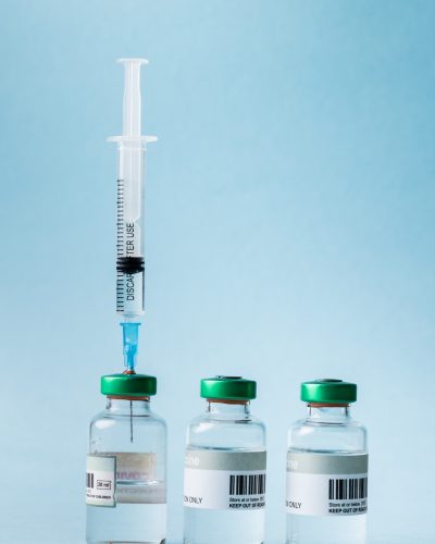 Close-up of syringe and vials arranged against blue background, copy space